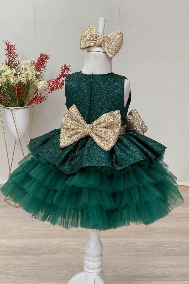 Back view of an elegant green sleeveless lurex fabric fairy dress that has gold sequin belt and bow and multi layered skirt