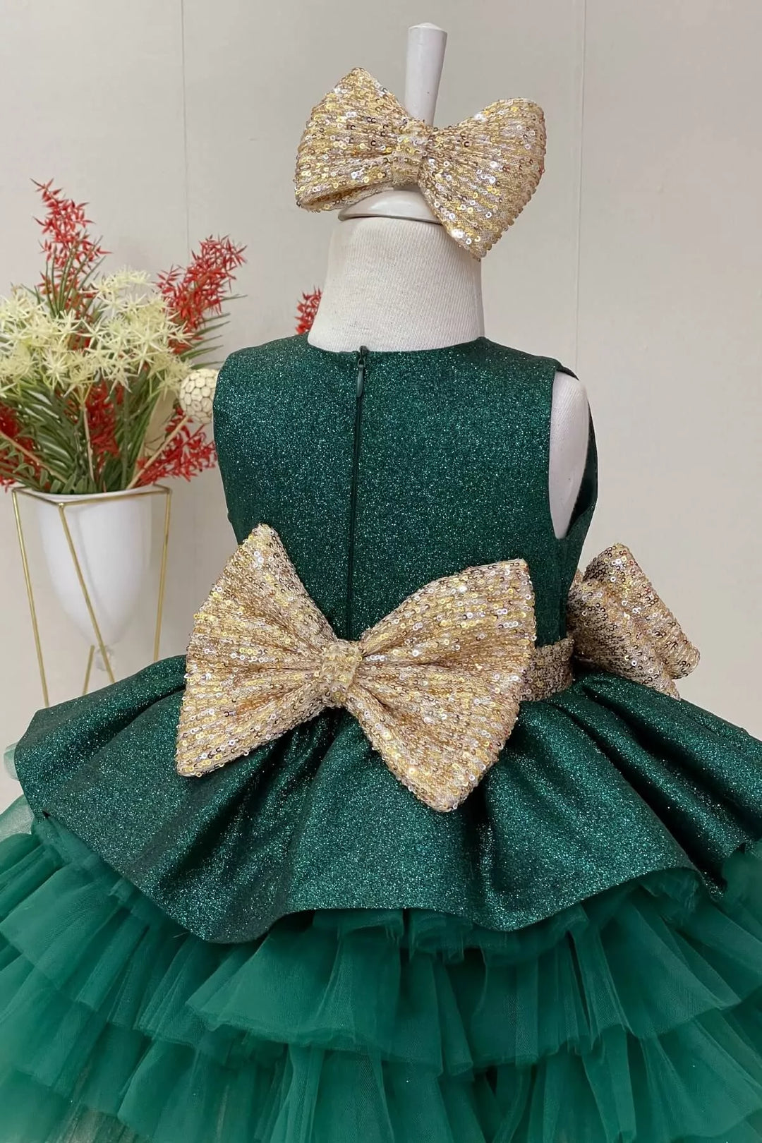 Back view of an elegant green sleeveless lurex fabric fairy dress that has gold sequin belt and bow and multi layered skirt