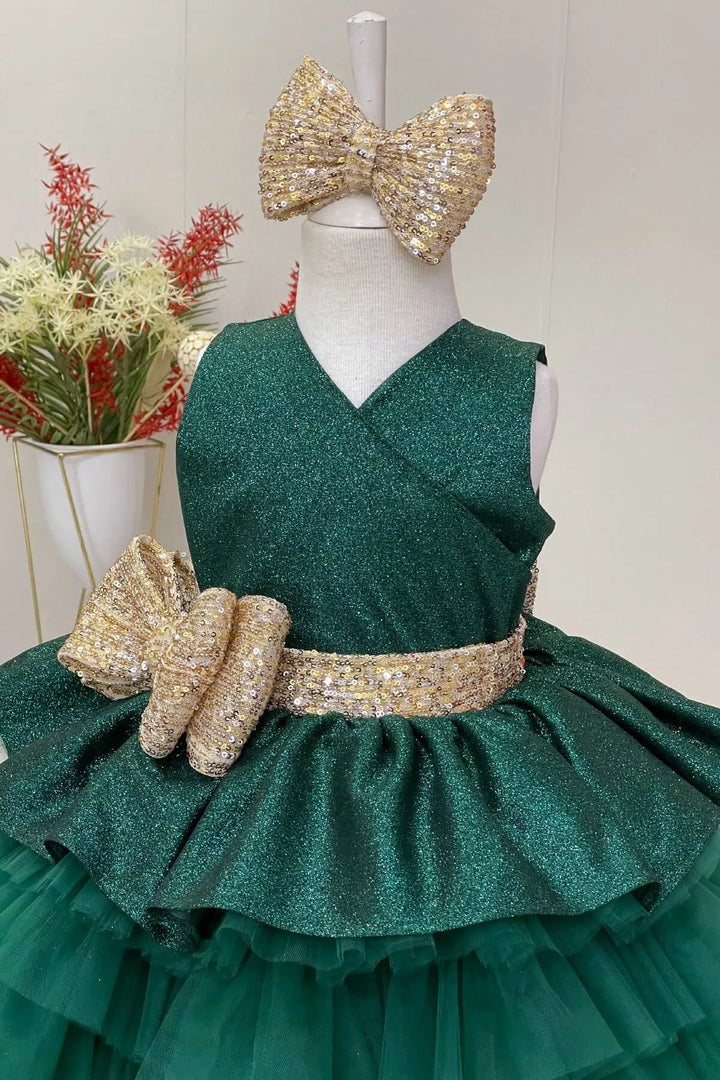 Close up view of an elegant green sleeveless lurex fabric fairy dress that has gold sequin belt and bow and multi layered skirt
