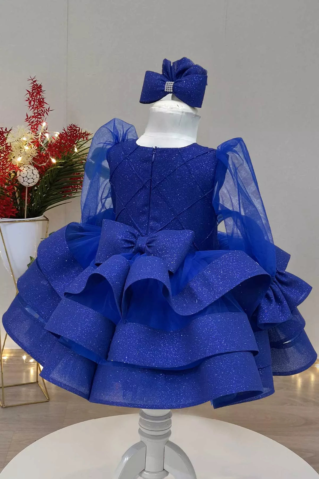 Back view of a sax blue long sleeve princess dress that has lurex brocade, tulle arms, bow, and multi layered knee length skirt