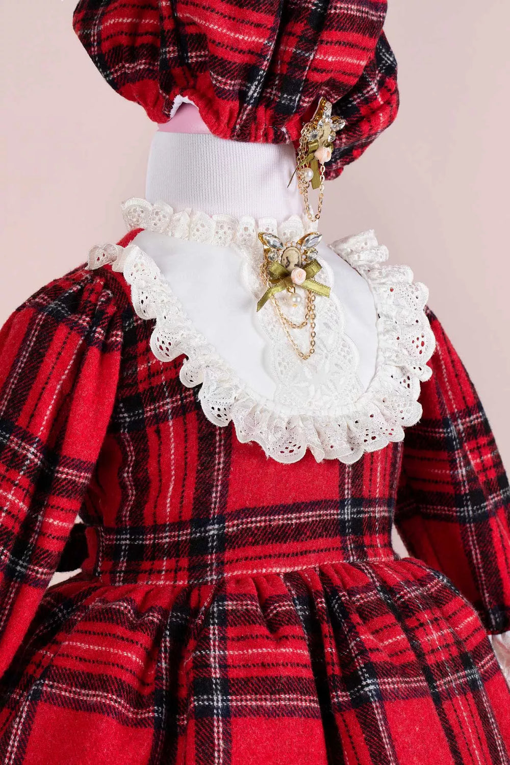 Close up view of a red plaid print velvet Christmas dress set that has long sleeves, hat, and brooch