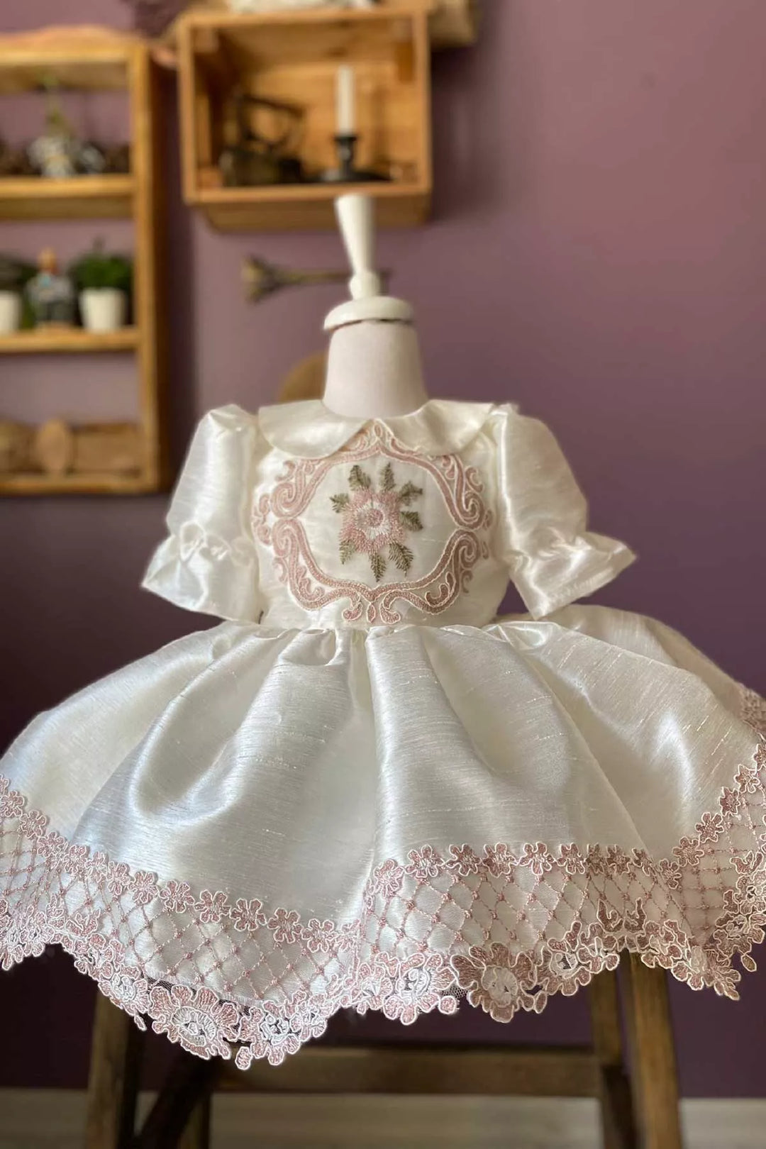 Close up view of a white vintage dress that has silk slub with embroidery and French lace, baby collar, shirred half sleeves, French lace on hems, and knee length skirt
