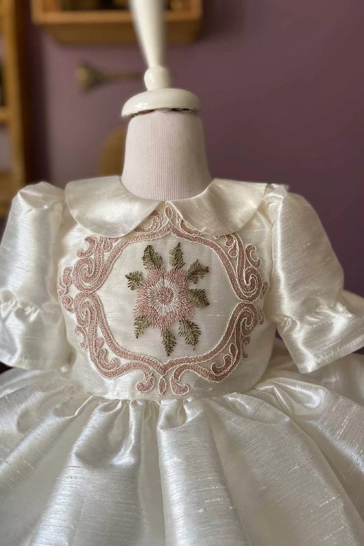 Close up view of a white vintage dress that has silk slub with embroidery and French lace, baby collar, shirred half sleeves, French lace on hems, and knee length skirt