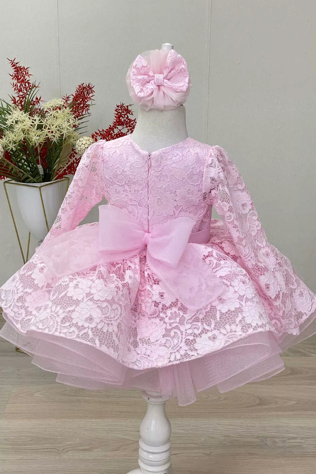 Back view of a pink candy girl dress that has long lace sleeves, floral lace, satin belt, grain tulle bow and grain tulle knee length skirt