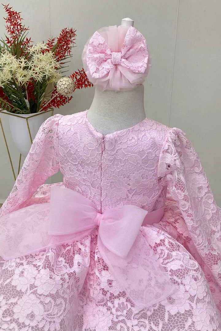 Back view of a pink candy girl dress that has long lace sleeves, floral lace, satin belt, grain tulle bow and grain tulle knee length skirt