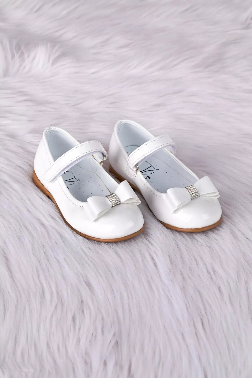 White toddler shoes that have crystal stone ornaments and bow tie