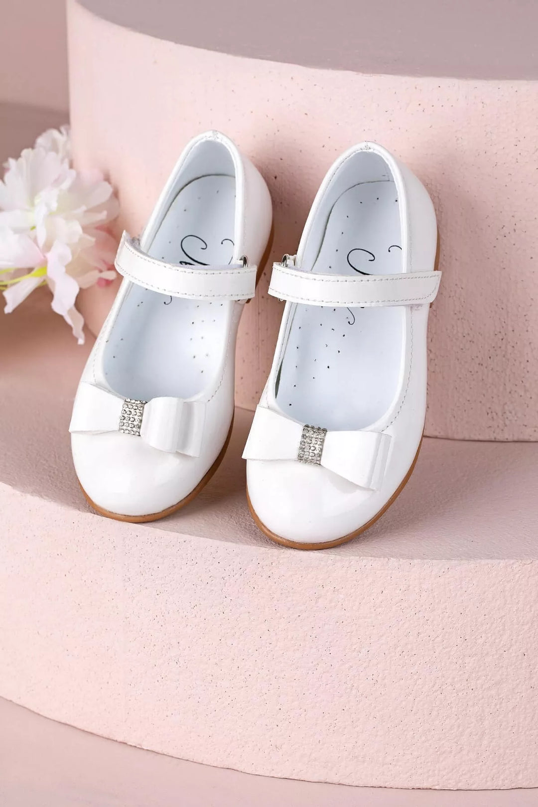 White toddler shoes that have crystal stone ornaments and bow tie