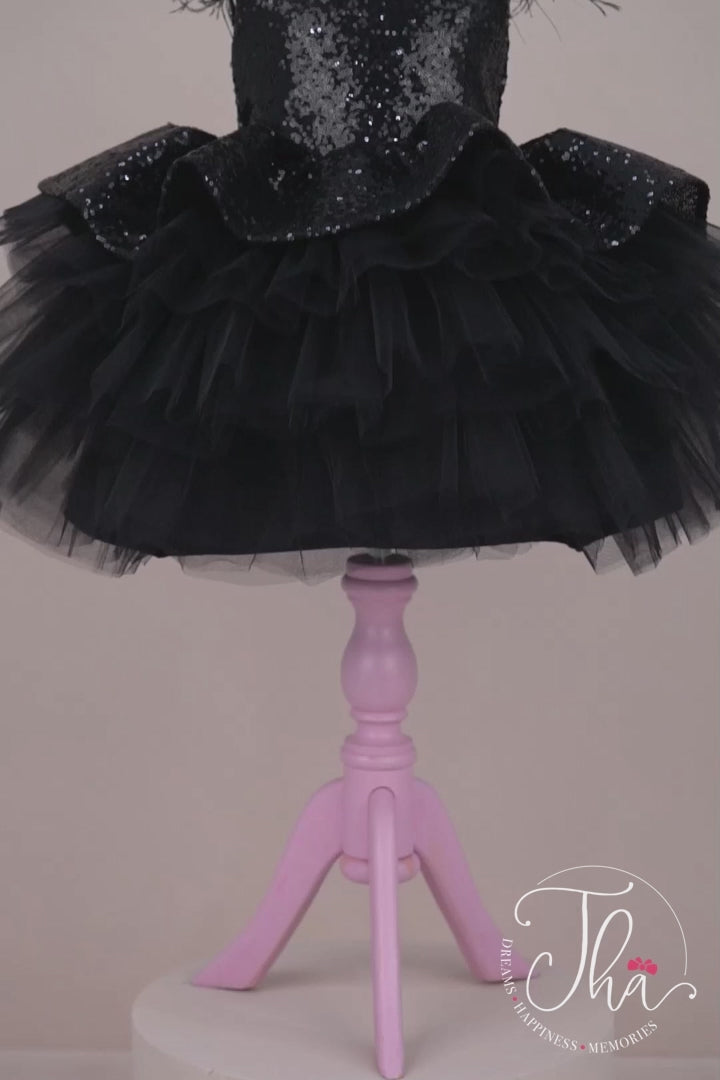 360° view of a black tutu princess dress which has cap sleeve, feathers on arms, sequin fabric top, bow, and layered skirt